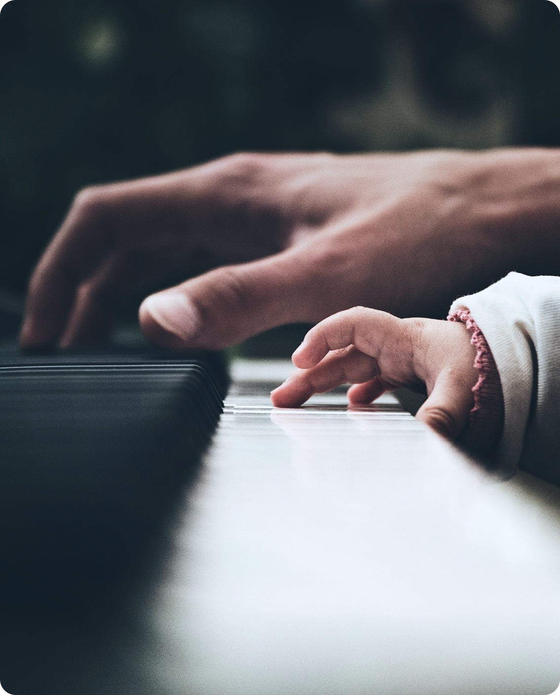 A parent and child's hands playing piano together
